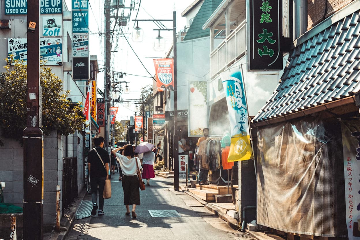 People walking on a popular street during the daytime surrounded by signs with Japanese writing, in the Shimokitazawa neighborhood of Tokyo.