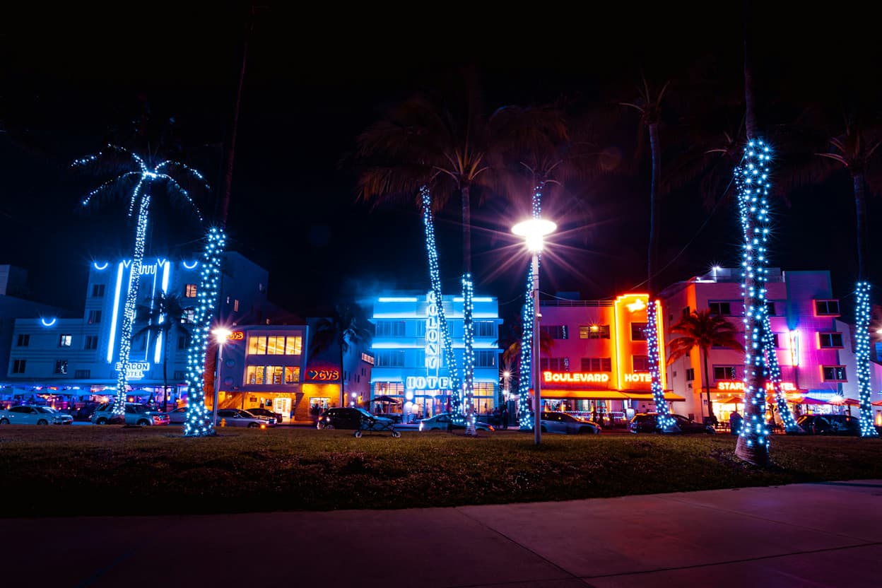 View from the beach of South Beach's art deco buildings and vibrant neon light signs during night time.