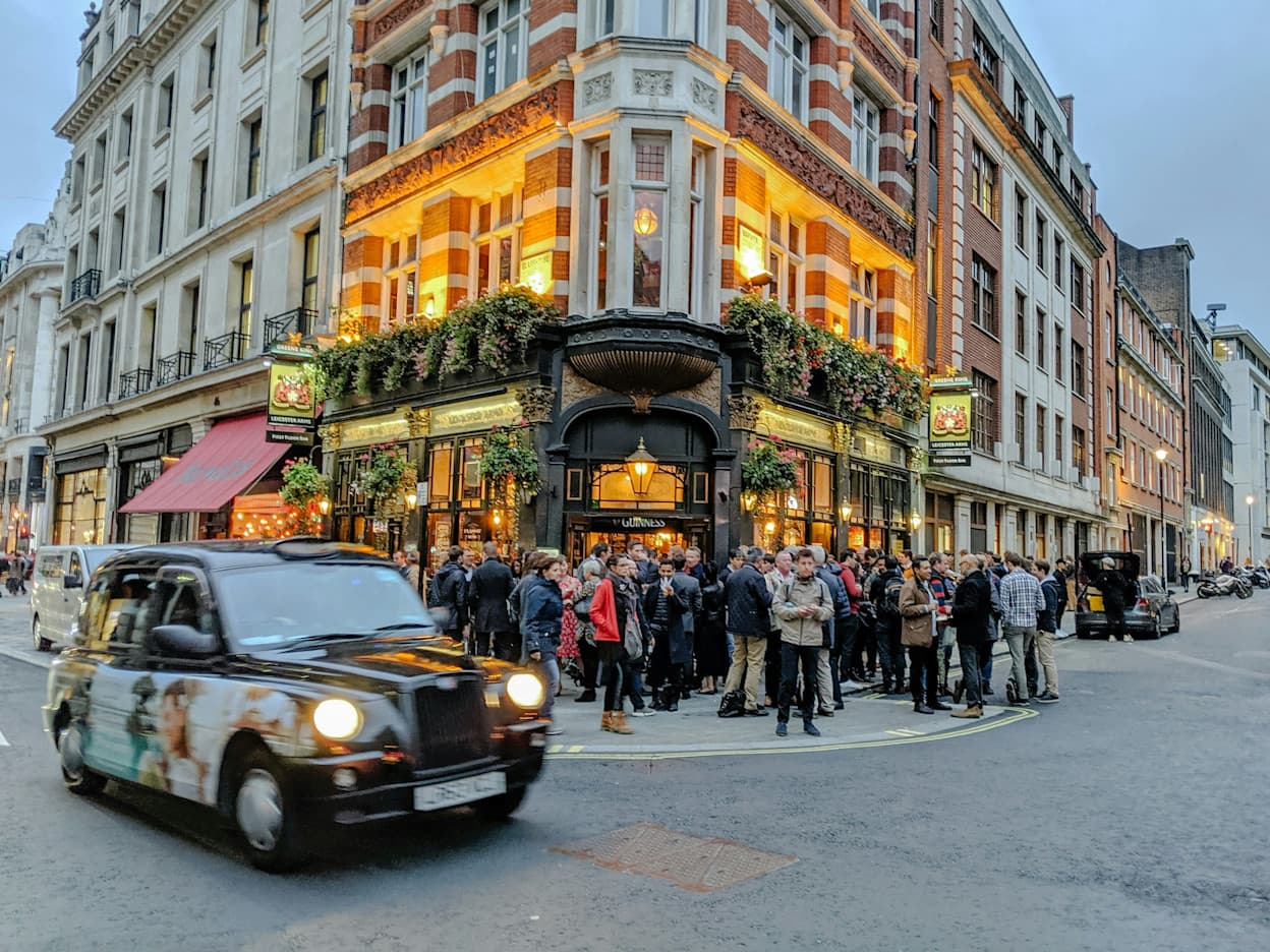 A black taxi is driving along a street corner at an intersection in Soho, London.