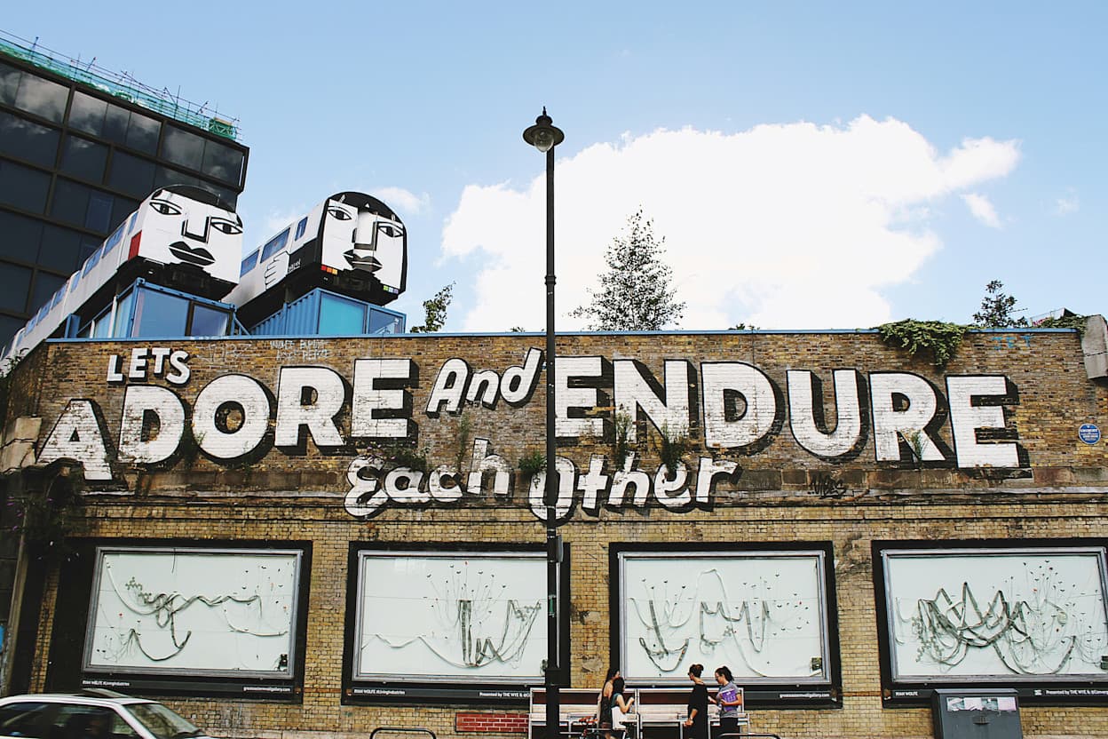 Brick building in Shoreditch, London with mural saying "Let's Adore and Endure Each Other" painted on the side