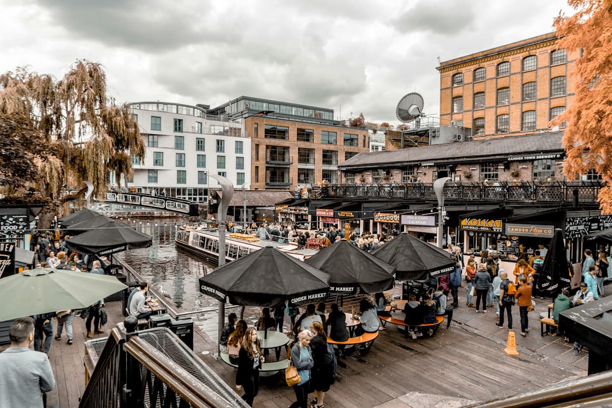 Umbrellas over outdoor tables along the river at Camden Market, in Camden, London with buildings in the background