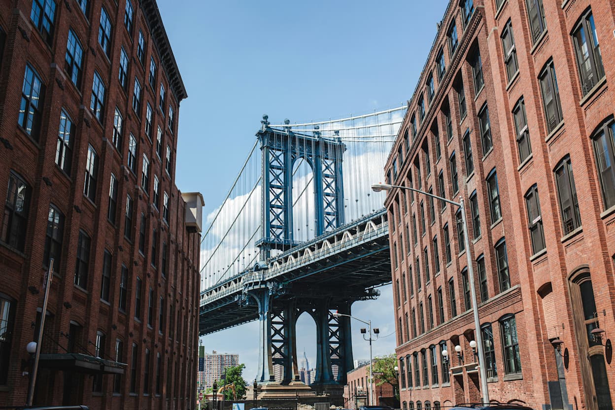 View of the iconic Brooklyn bridge through buildings in the DUMBO neighborhood of New York City.