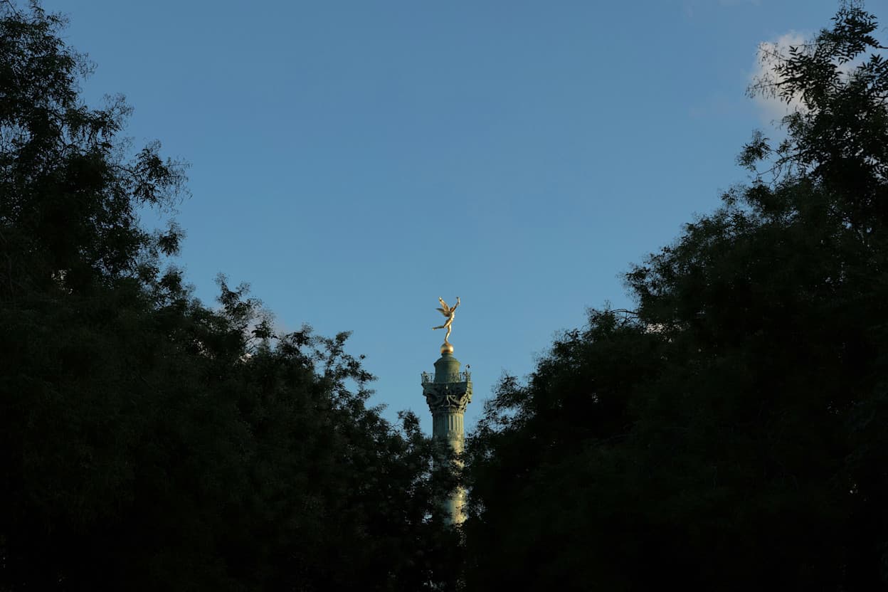 The gold peak of the Place de la Bastille statue is seen above a canopy of trees.