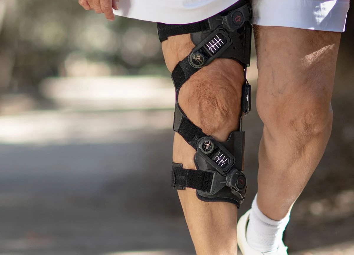 Close-up of a person’s leg wearing a black knee brace while walking outside.