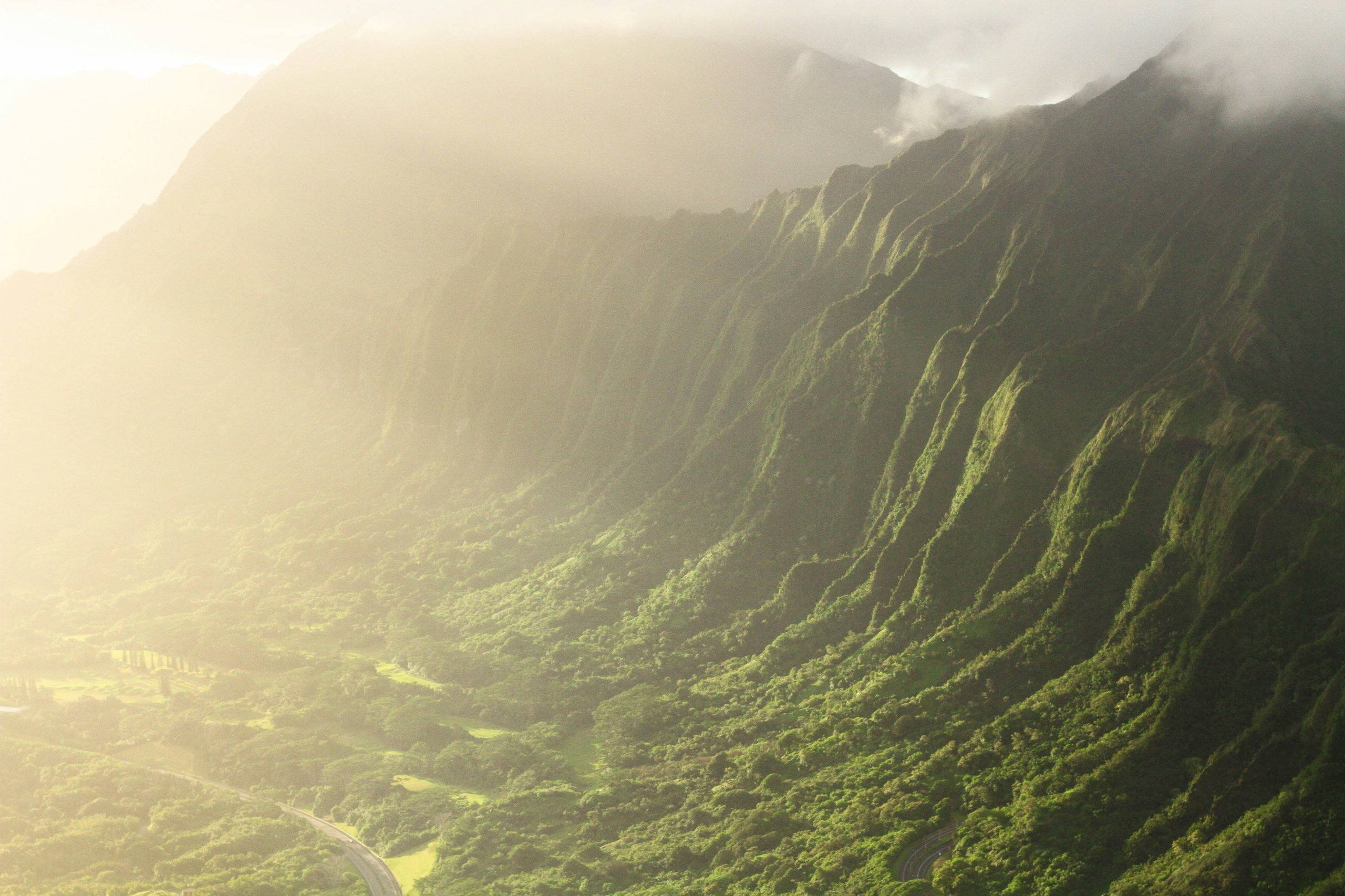 Sunlit green mountain ridge with deep valleys and misty clouds.