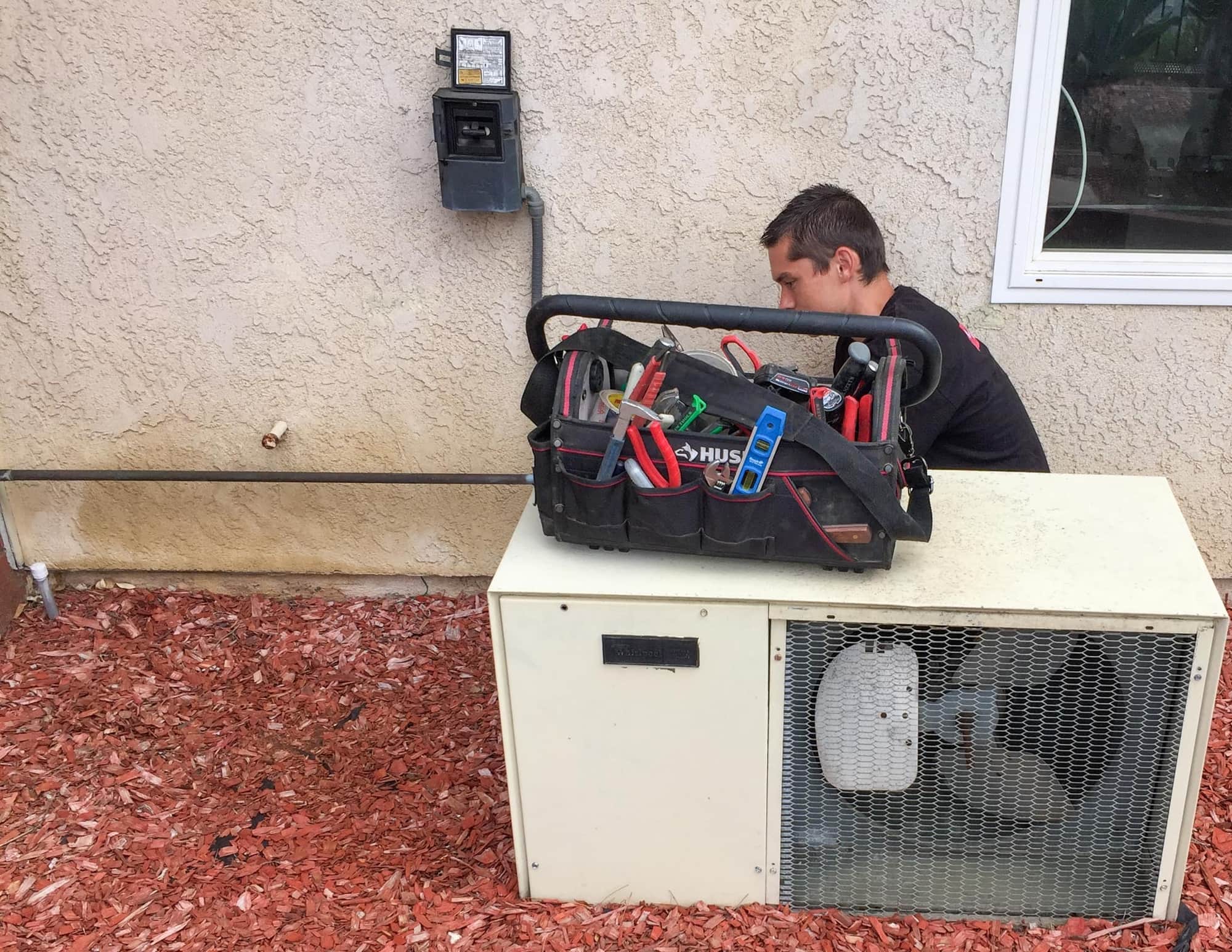 HVAC technician performing AC repair on an outdoor air conditioning unit at a residential home.