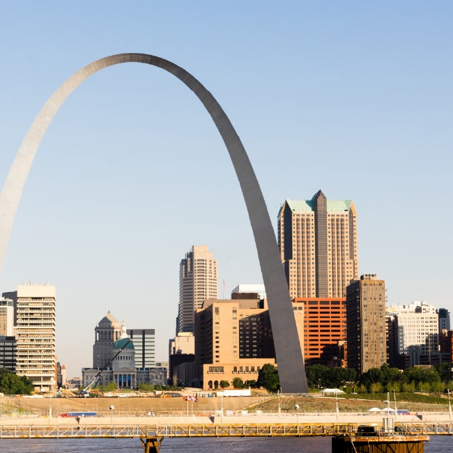 The Gateway Arch standing tall over the downtown skyline of St. Louis, Missouri, with a clear blue sky.