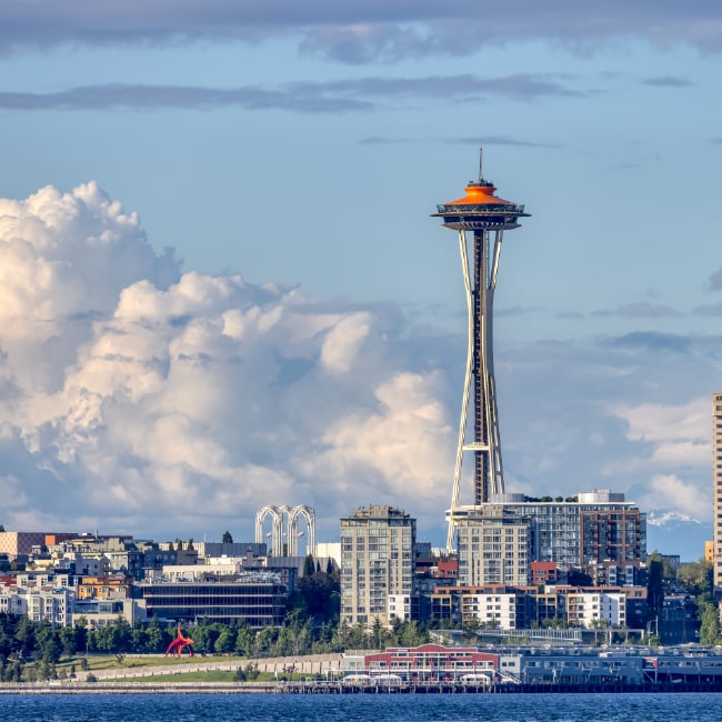 Seattle skyline featuring the Space Needle with a partly cloudy sky and waterfront buildings.