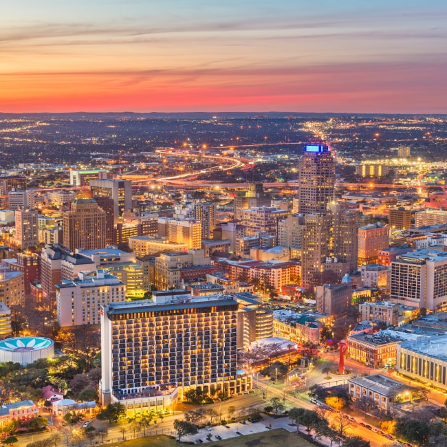 Aerial view of a cityscape at sunset with illuminated buildings and roads.