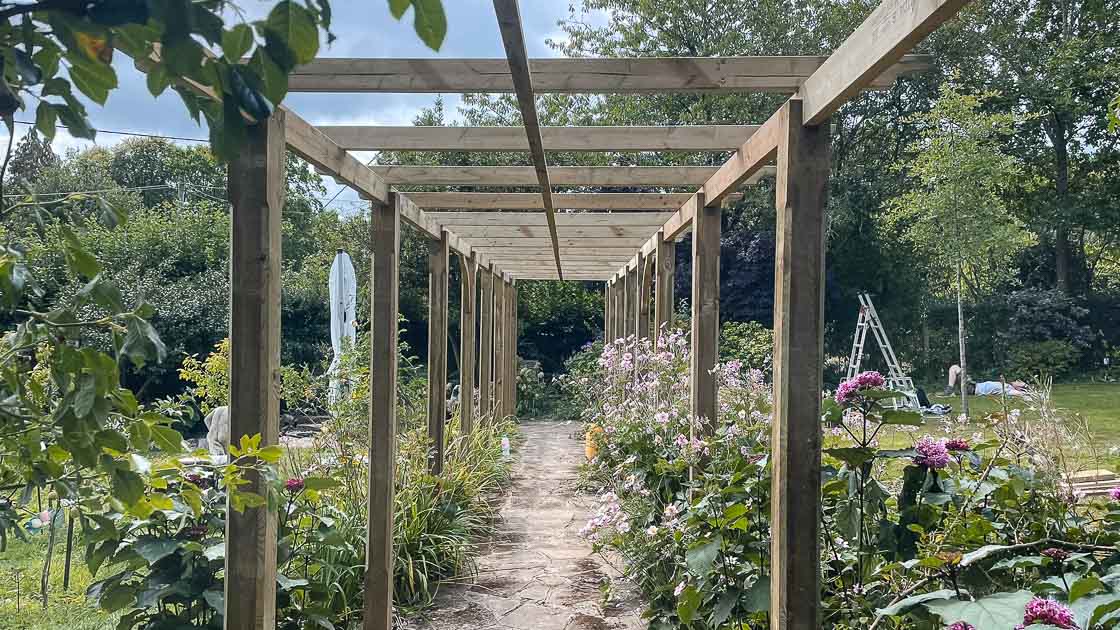 Long timber pergola walkway with climbing plants and open roof beams, creating a shaded garden path in East Grinstead.