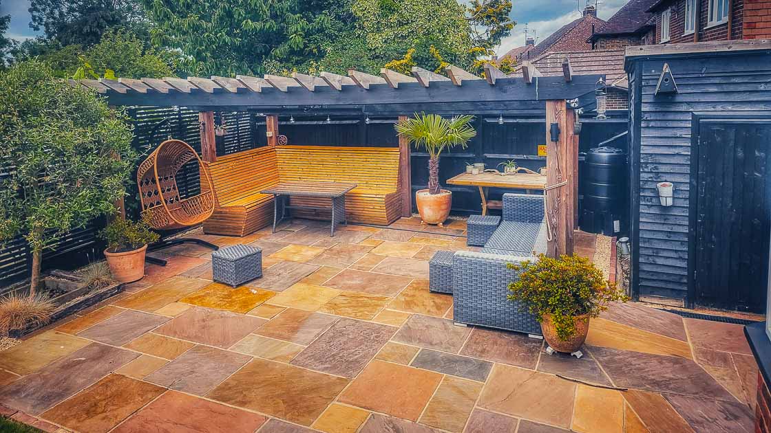 Modern garden seating area with timber pergola, slate fencing, and sandstone patio in a landscaped East Grinstead garden.