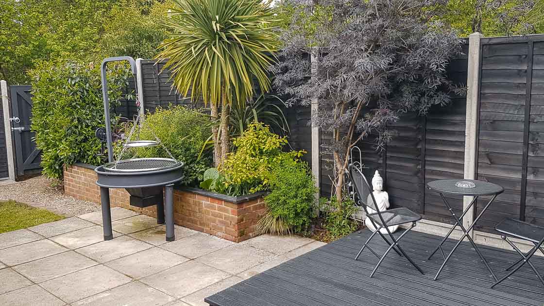 Modern black composite panel fencing surrounding a garden patio with tropical plants and seating area.