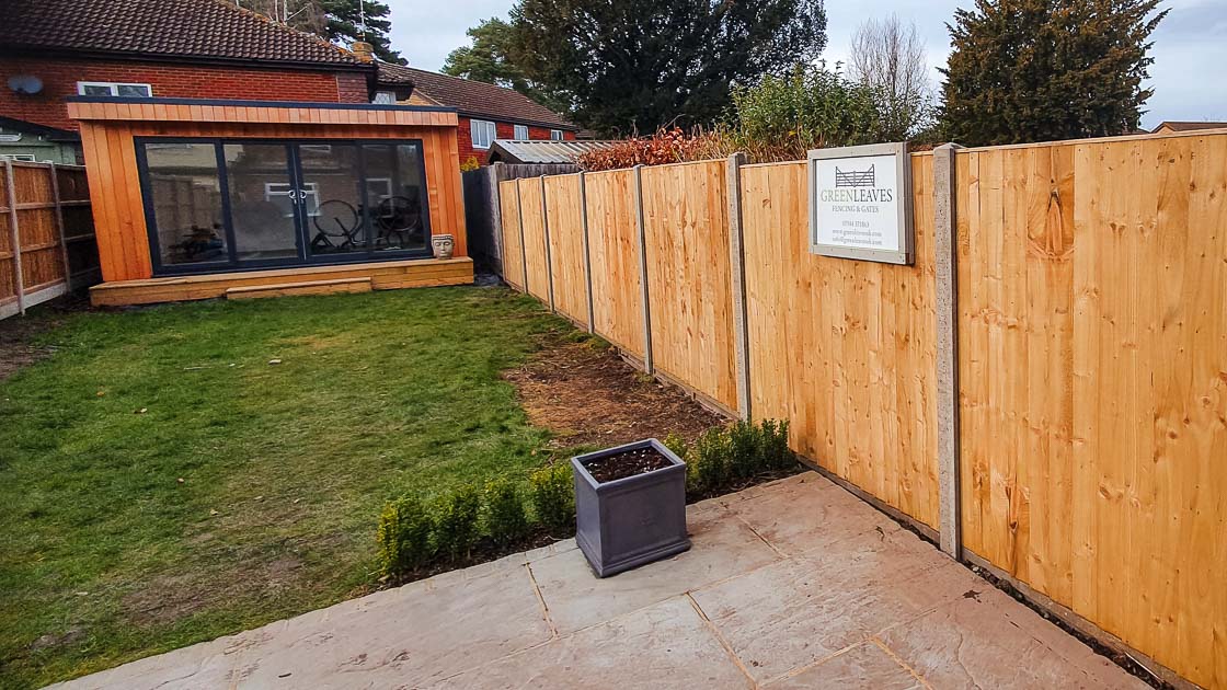 Timber panel fencing with concrete posts, installed along a lawn and paved area beside a modern home in East Grinstead.