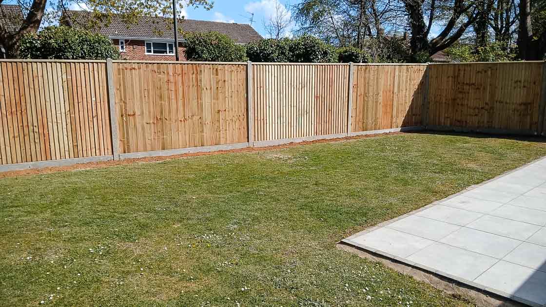 Closeboard fence with concrete posts and gravel boards enclosing a spacious lawn beside a new patio area.