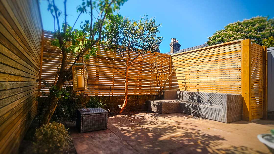 Contemporary slatted timber fencing surrounding a stylish patio area with warm-toned paving and seating.