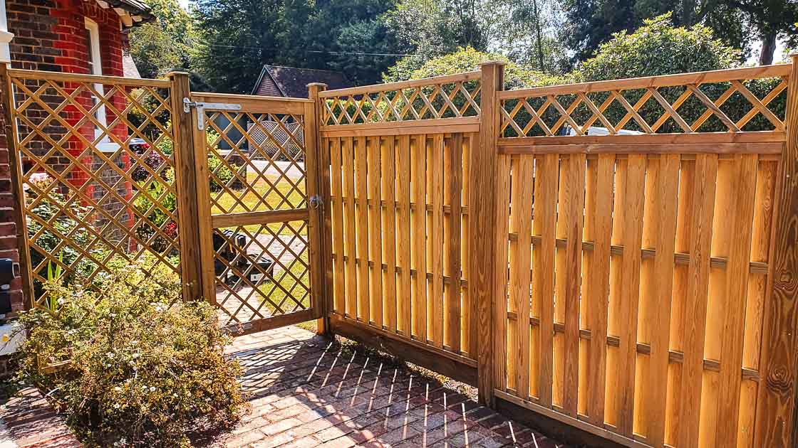 Golden timber fence with diamond-lattice trellis panels and matching gate enclosing a landscaped garden.