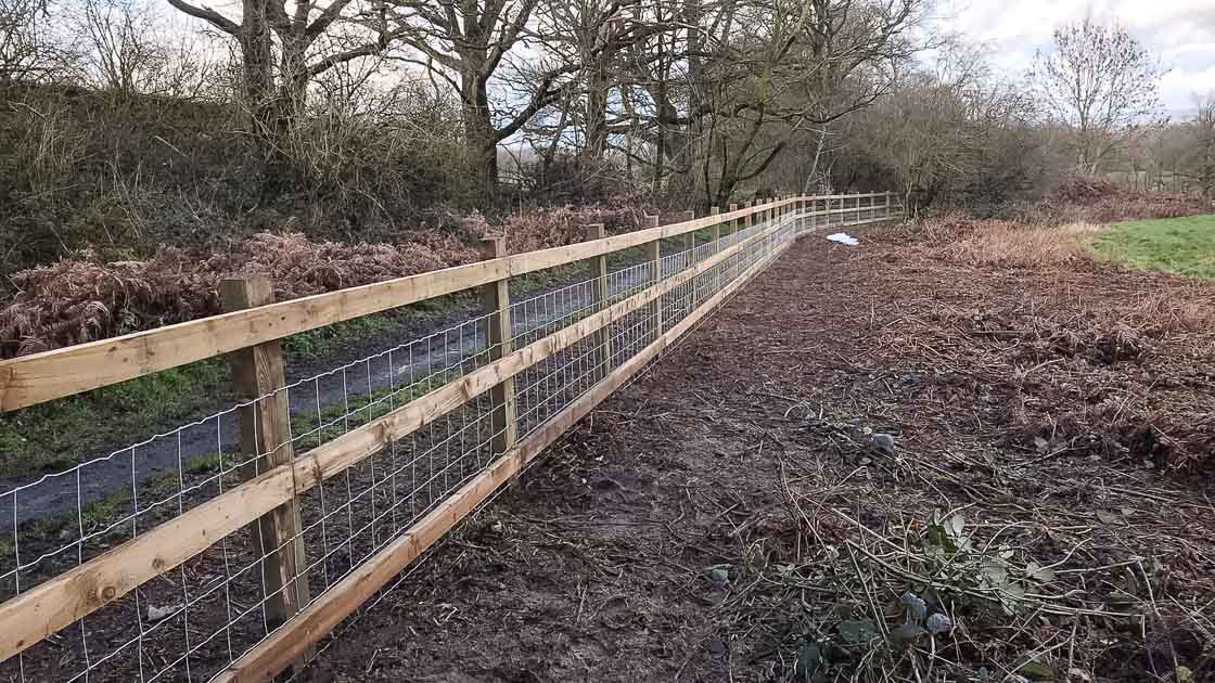 Timber post and rail fencing with wire mesh lining a rural field edge in West Sussex countryside.