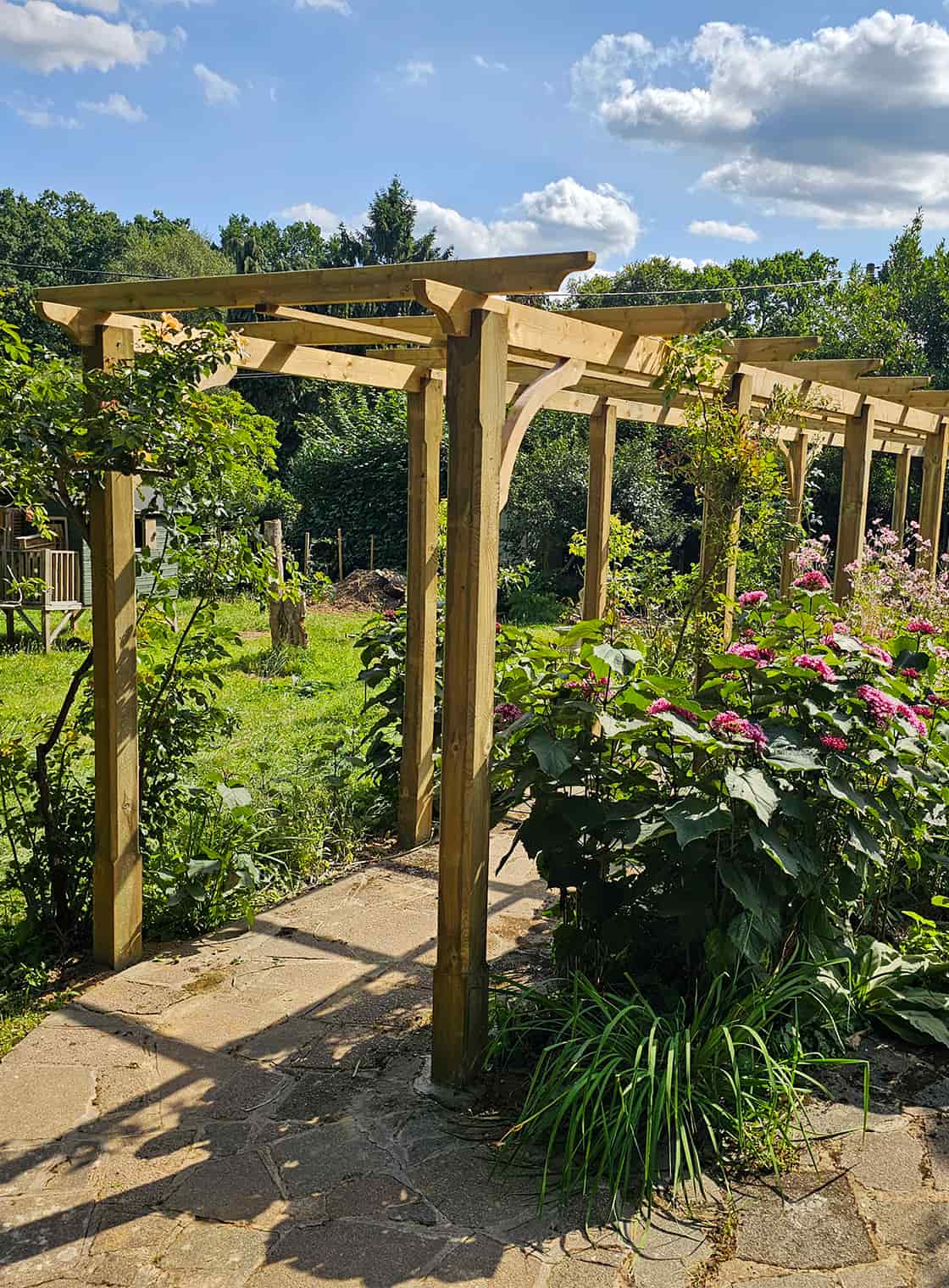 Timber driveway gate installed at a residential property, framed by hedging and garden planting.