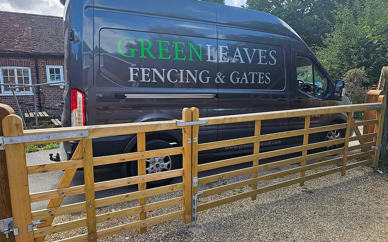 Wooden driveway gate in front of a dark van with Green Leaves Fencing & Gates branding, parked beside a brick house.