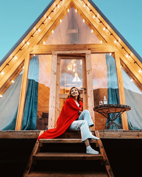 Photo of woman enjoying her vacation, sitting on a deck outside of an A-Frame cabin