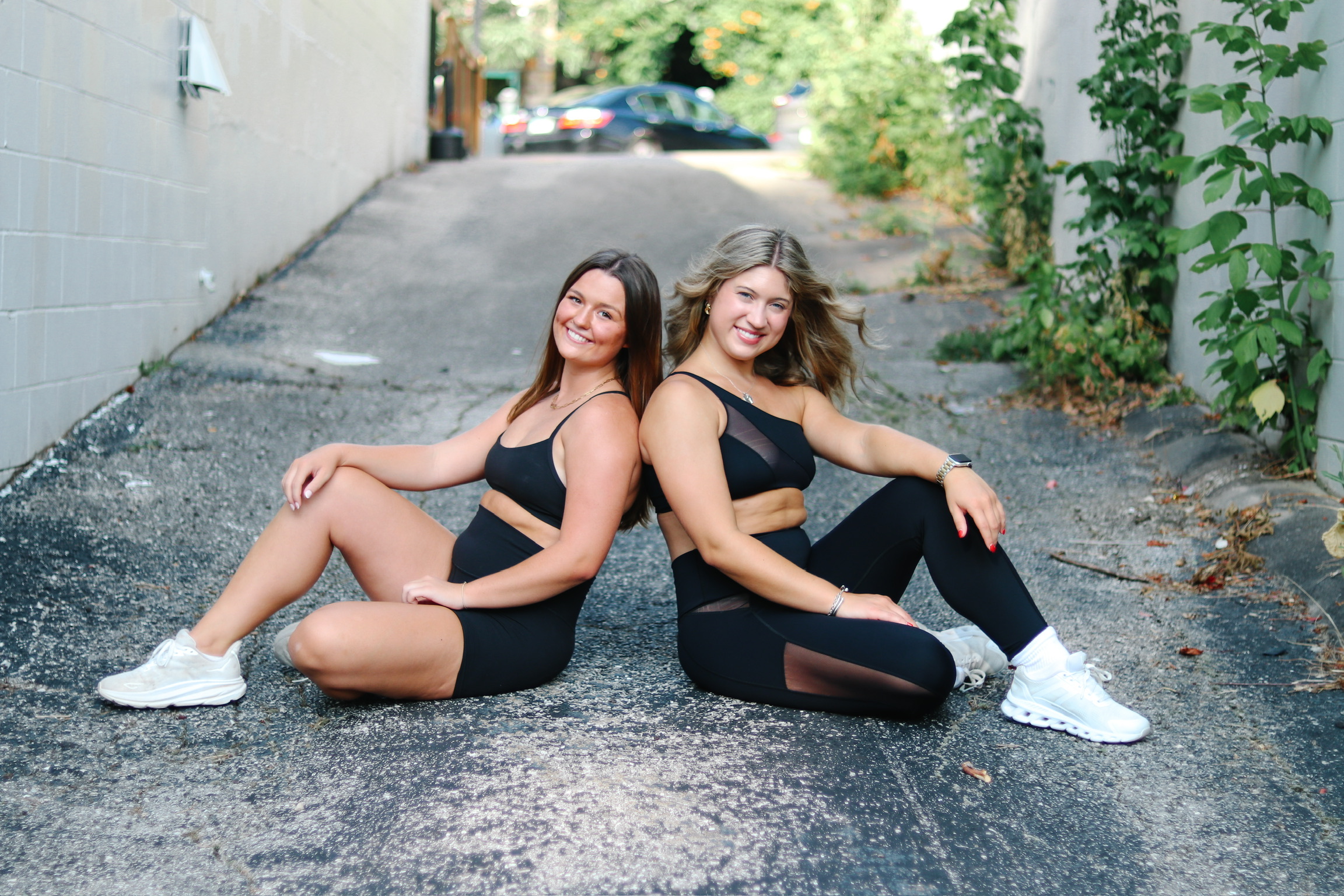 Ladies sitting back to back in alley smiling