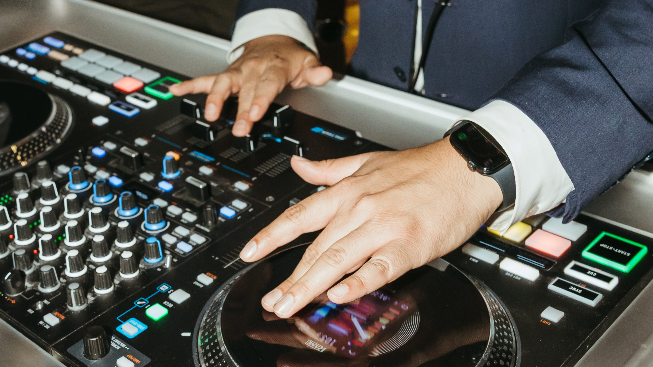 DJ in a suit manipulating knobs and a turntable on a professional music mixing console.