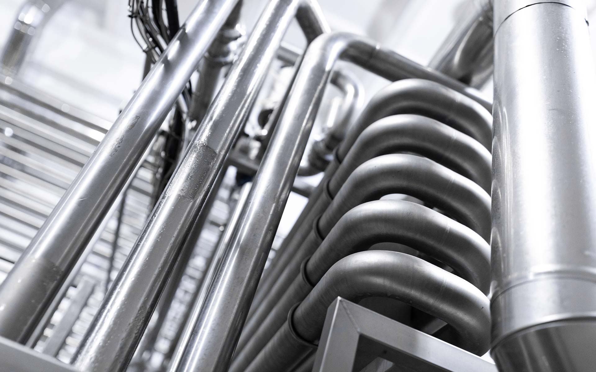 Close-up view of shiny industrial metallic pipes arranged in parallel and curved formations.