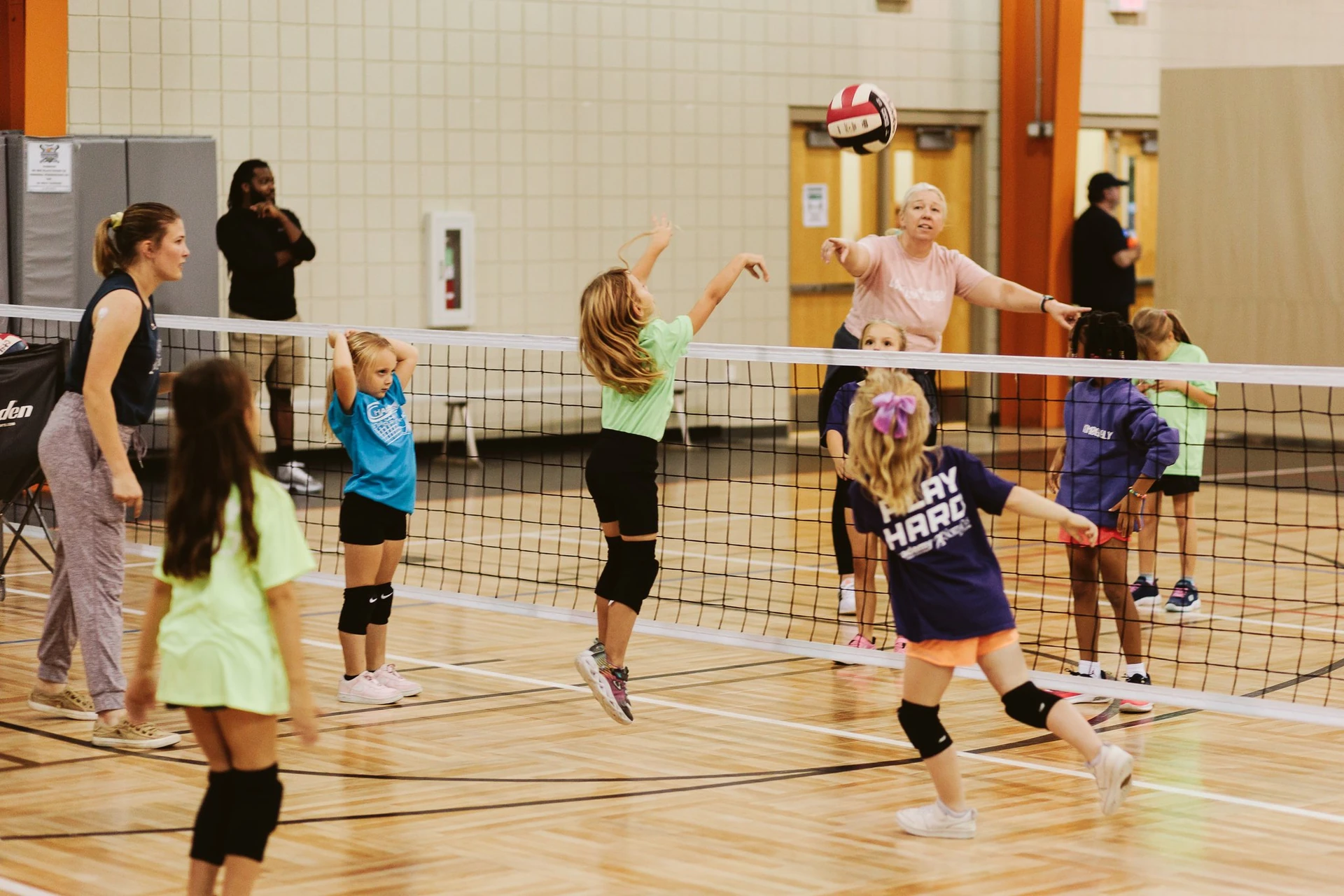 Young athletes learning to volley over the net with the help of coaches during a youth volleyball session at CSP.