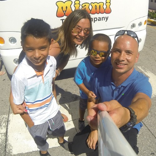 Famiglia sorridente di quattro persone che si fa un selfie davanti a un autobus della Miami Tour Company