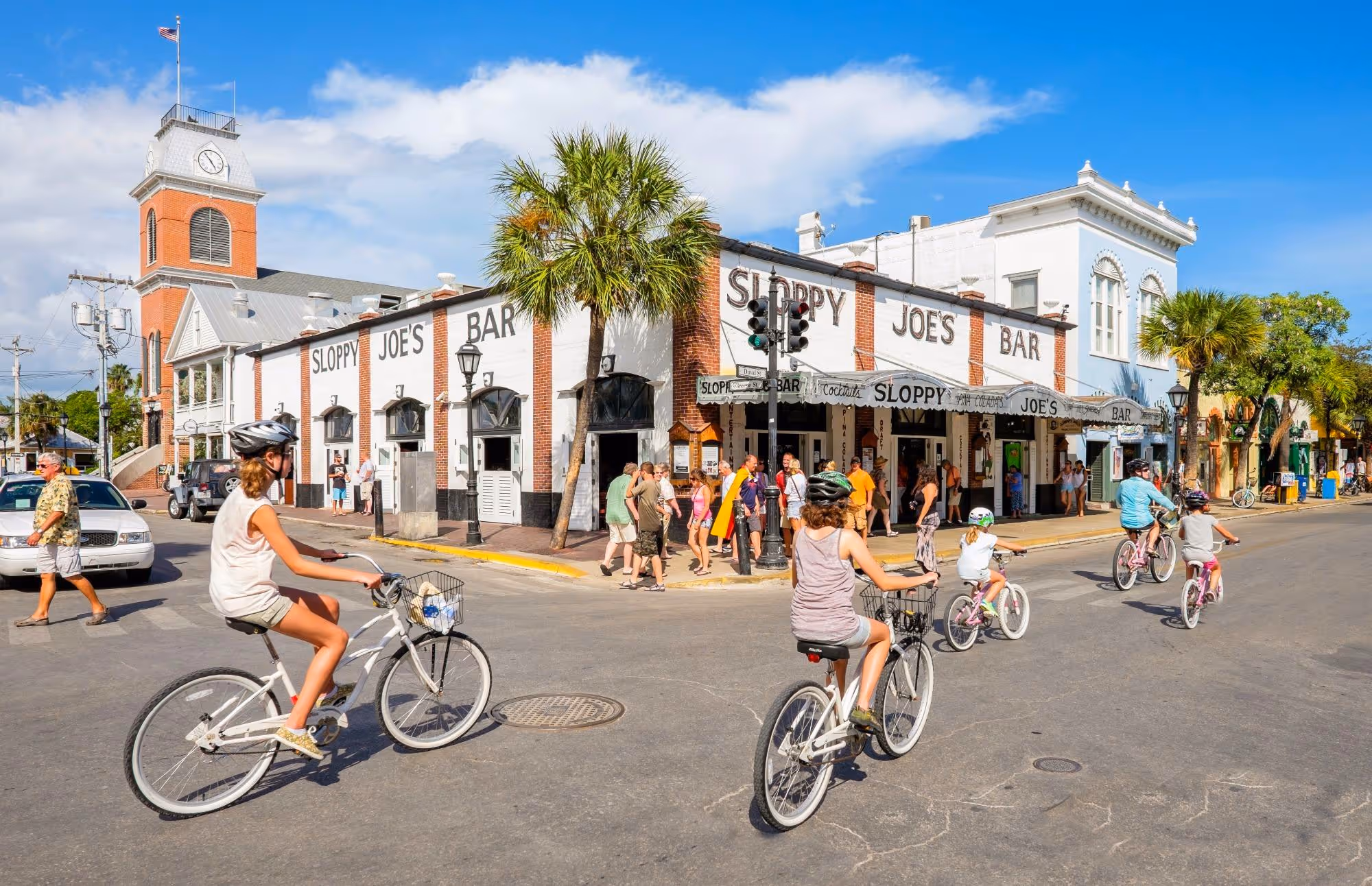 4 people riding bikes past Sloppy Joes Bar on a sunny day