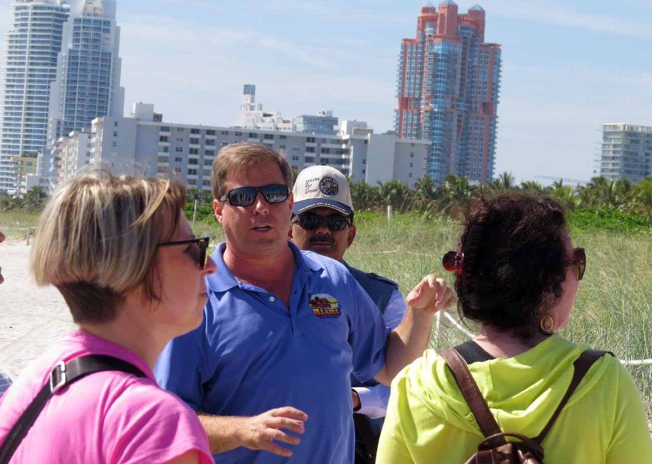 Tour guide in a blue shirt talking with two ladies on the beach with Portofino Tower in the background