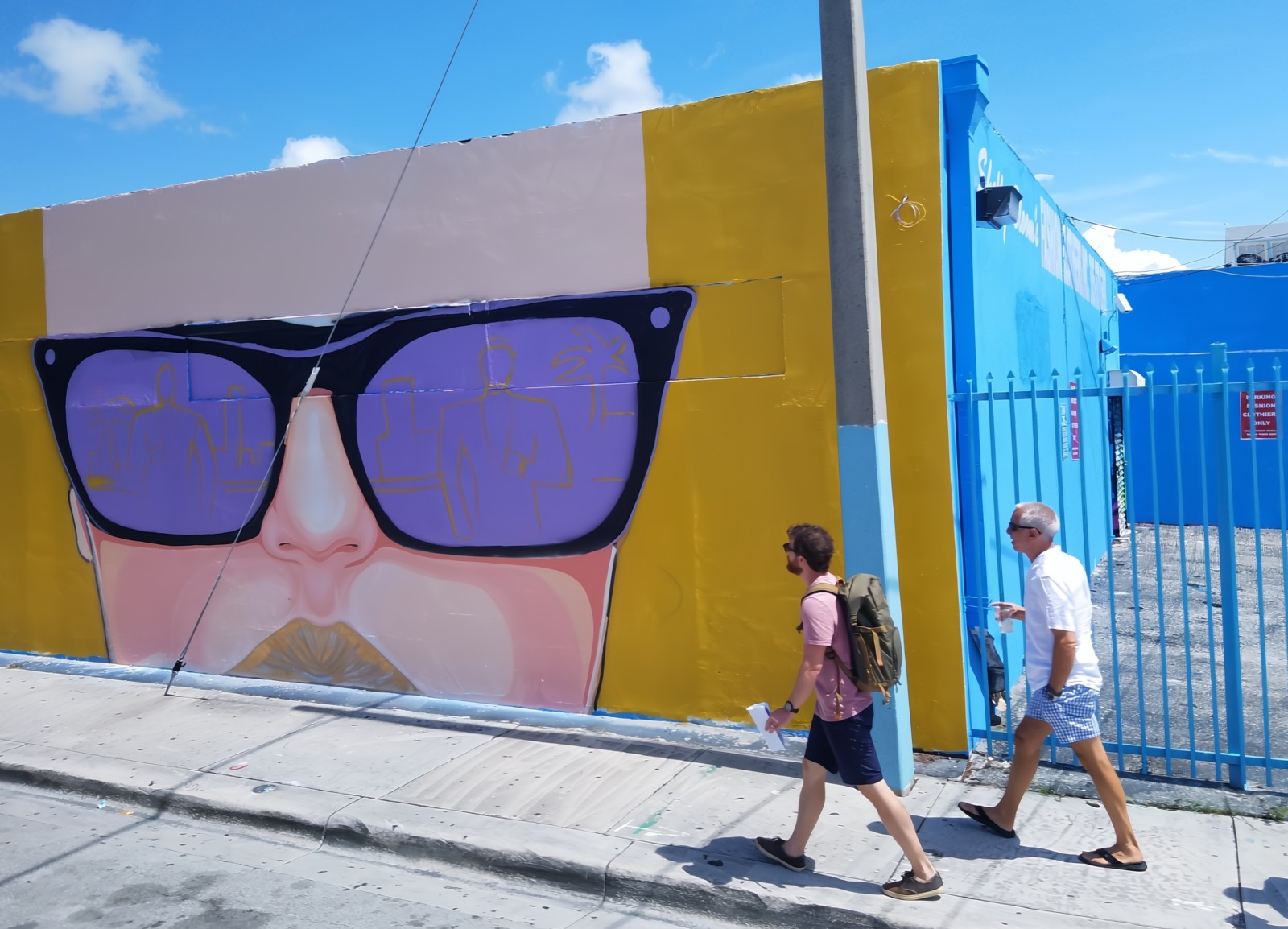 Two young men walking around the Street Art District passing a mural of an exotic women wearing sunglasses