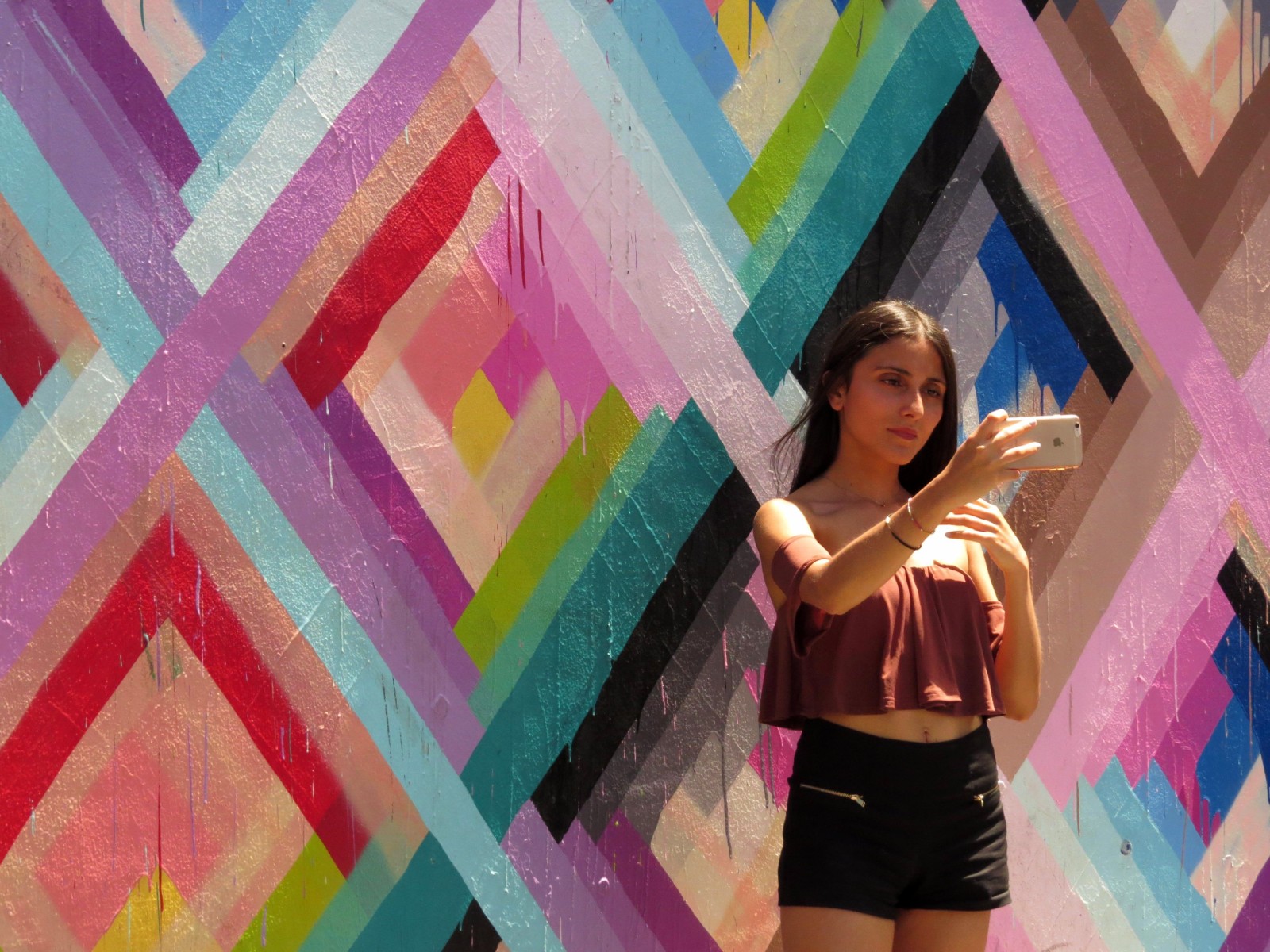 Beautiful women taking a selfie in from of a colorful mural with diamond shapes