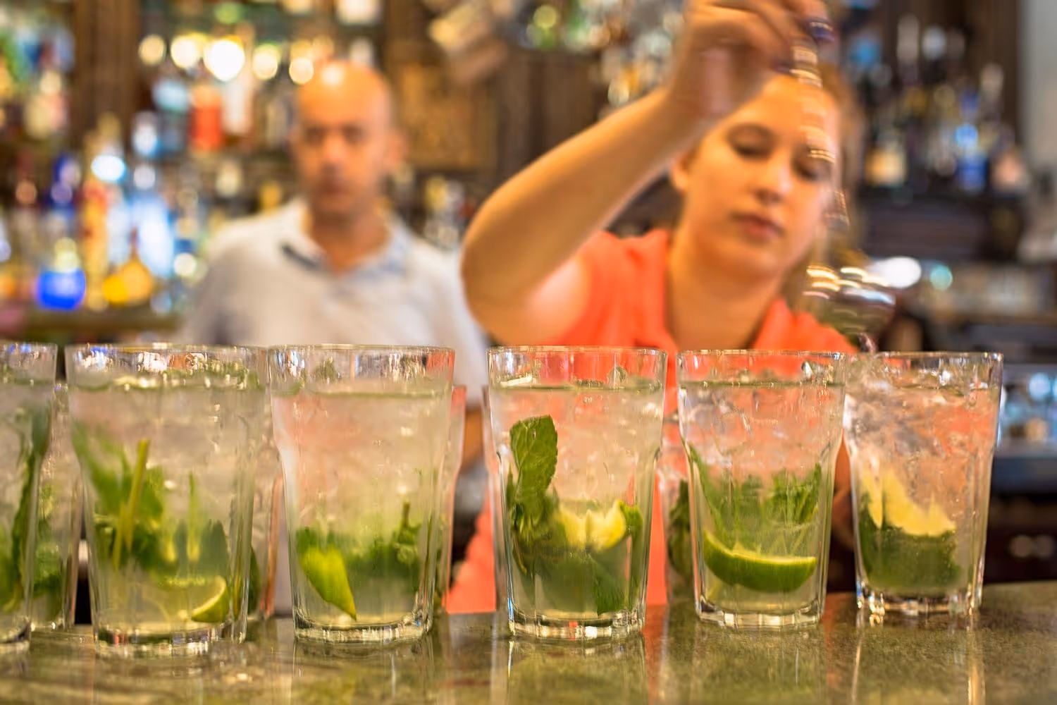 Close-up of a female bartender mixing five mojitos, with fresh mint and lime in each glass
