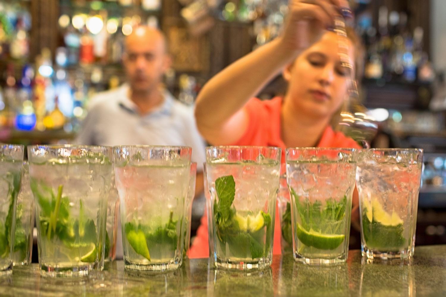 Close-up of a female bartender mixing five mojitos, with fresh mint and lime in each glass