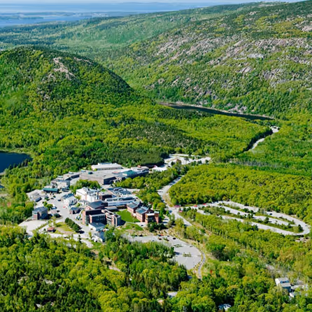 Aerial view of Jackson Laboratory campus nestled in forested hills of Bar Harbor, Maine with buildings surrounded by green landscape and water