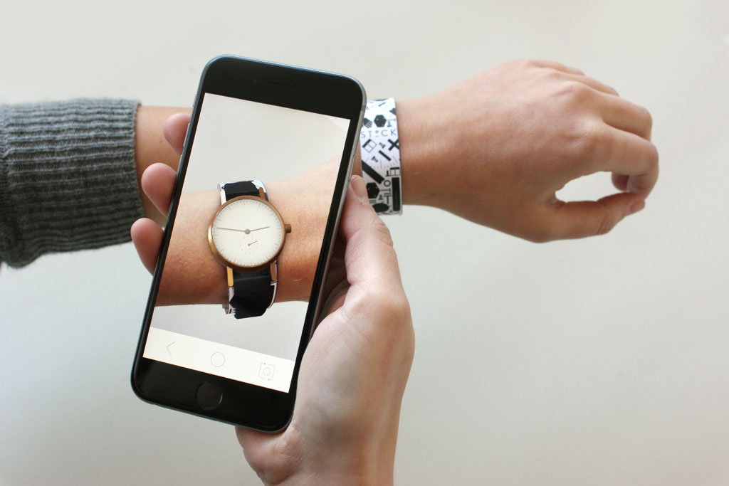 A photo of the iphone interface viewing the Stock Watches AR app experience. A person wears a print-out wrist strap and an iPhone visualises a watch on the wrist.