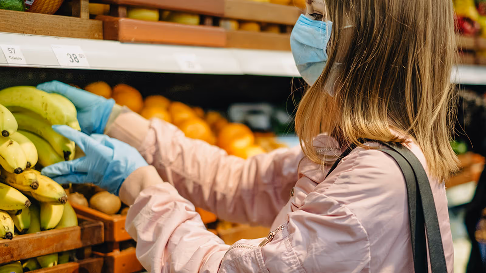 A woman wearing a face mask and gloves is picking oranges.