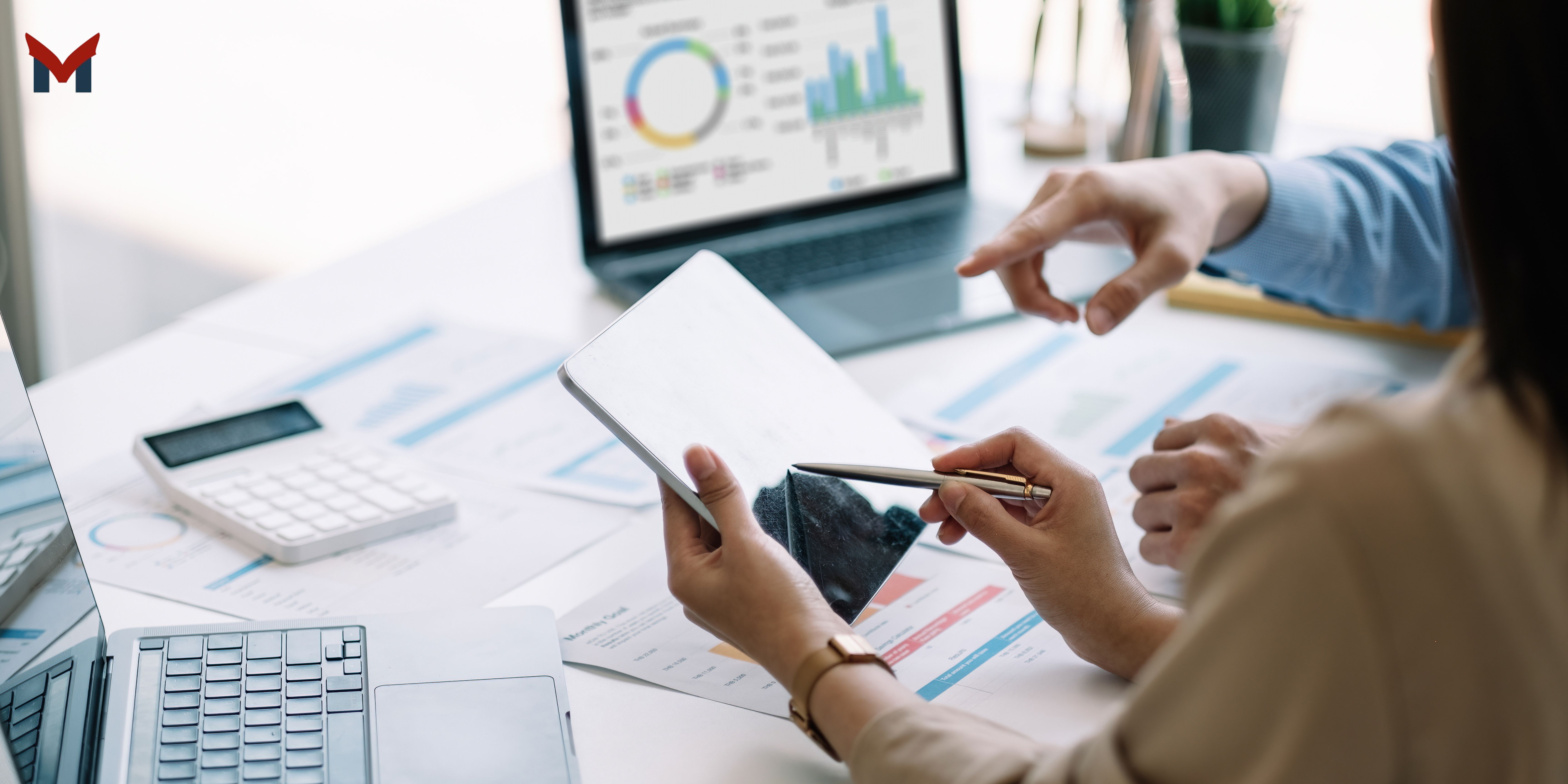 One person is holding a tablet and pointing at it with a pen, while the other gestures toward it — classic “let’s talk numbers” moment.