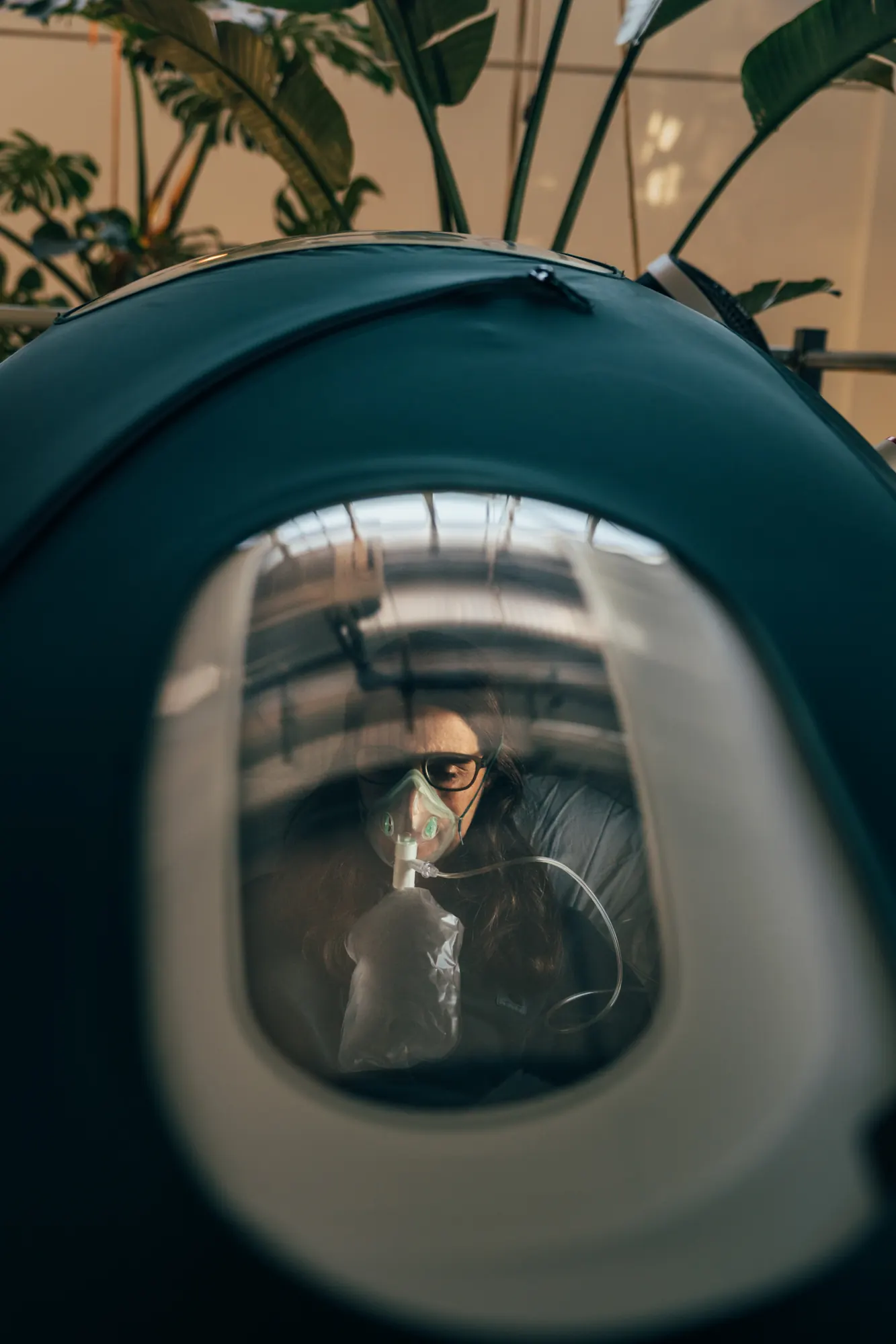 A member wearing an oxygen mask inside a Breathe hyperbaric chamber, seen through the chamber window
