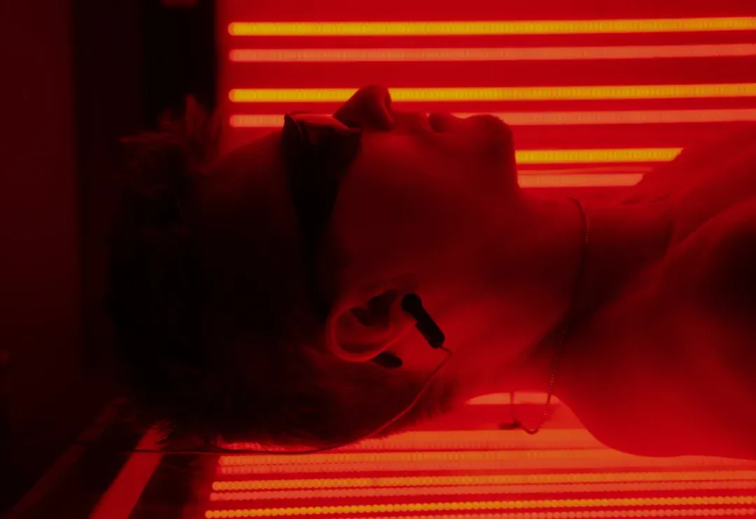 A member lying in the red light bed while using an Alpha-Stim unit