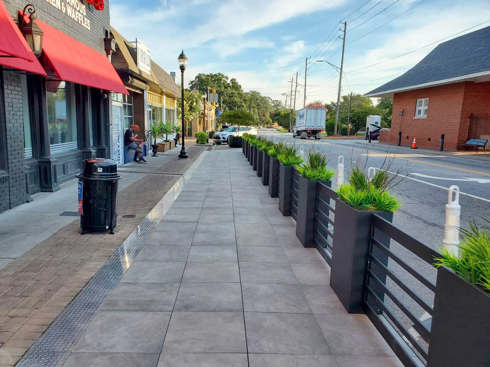 A sidewalk lined with planters beneath a vibrant red awning, creating a welcoming outdoor atmosphere.
