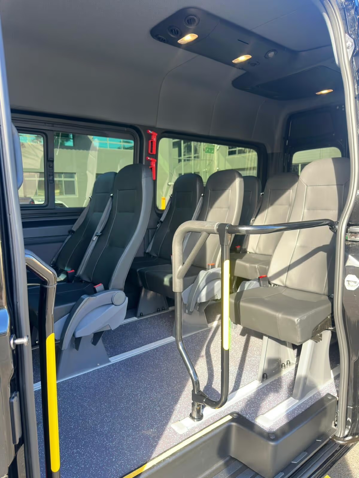 Minibus doorway with a grab rail and rows of grey leather seats