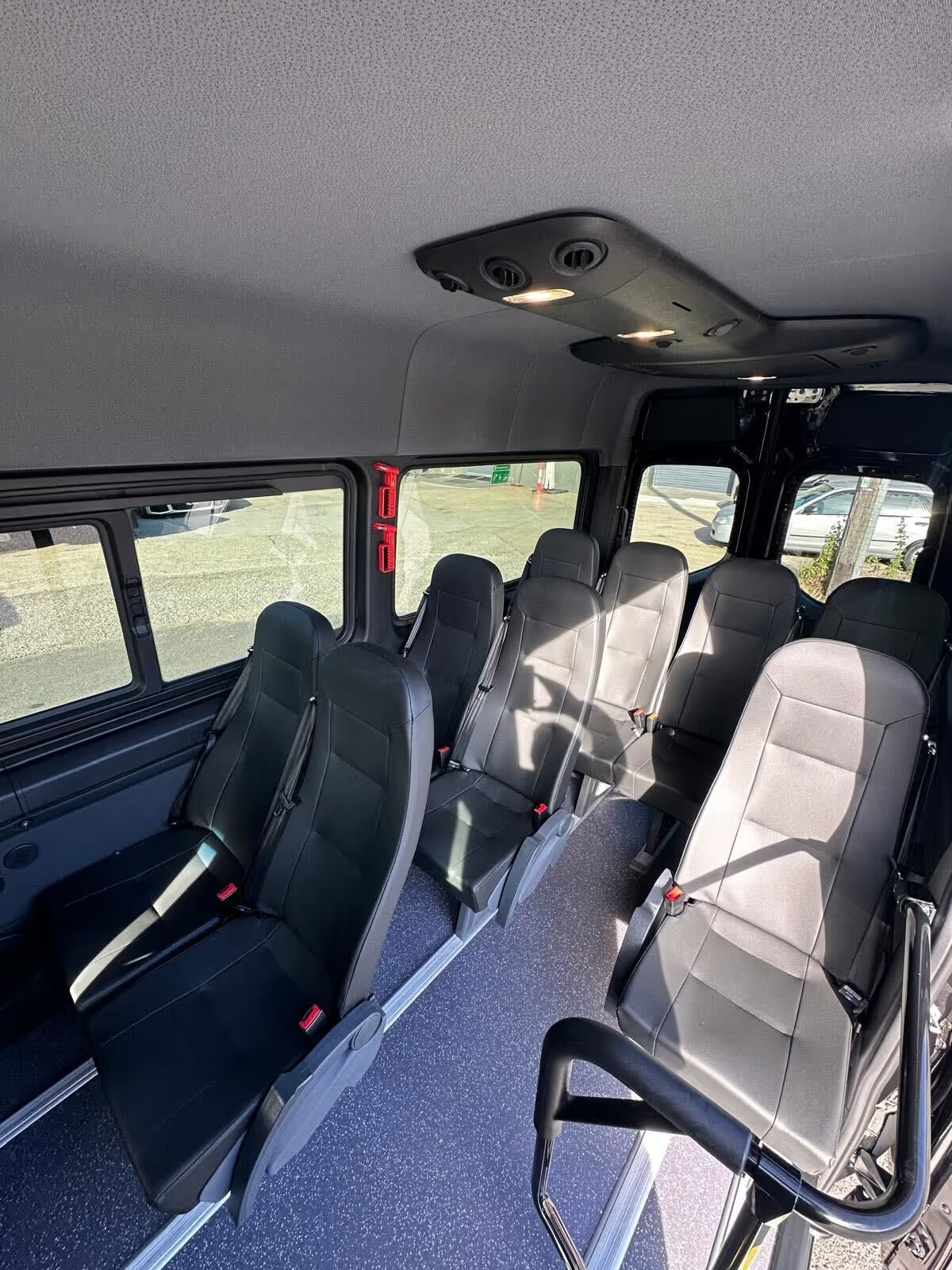 Rows of black leather minibus seats with seatbelts and large side windows
