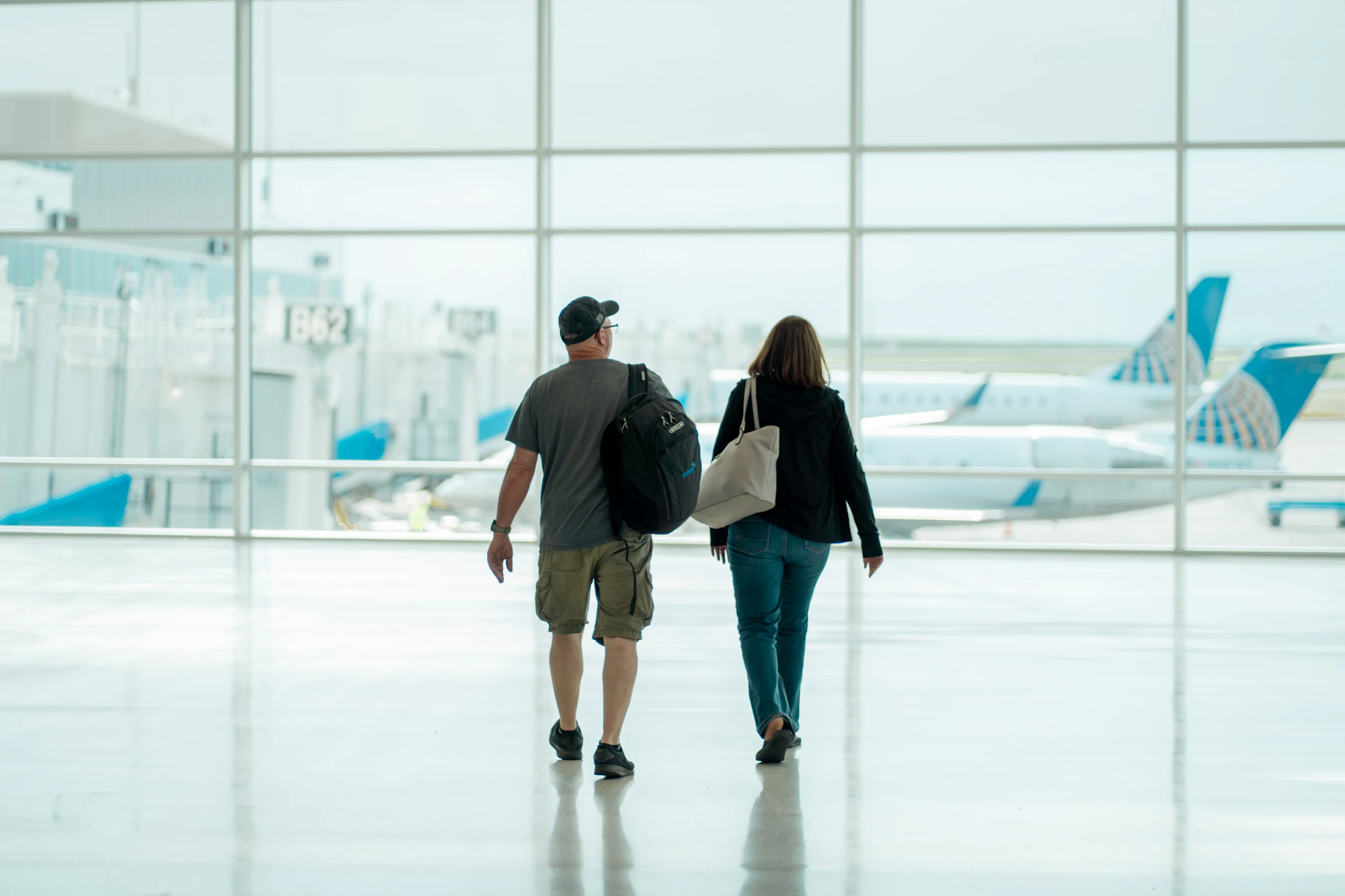 Two travellers with bags walking through an airport terminal towards the gates