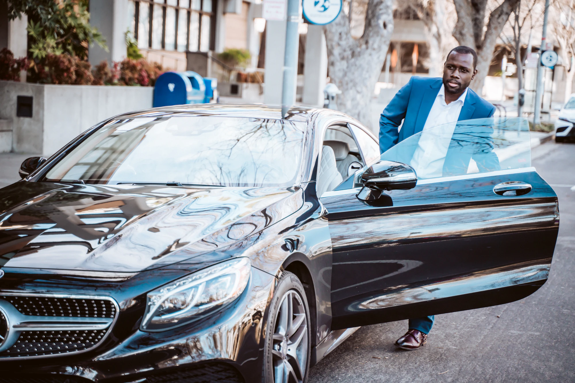 A businessman in a blue suit steps out of a black Mercedes-Benz