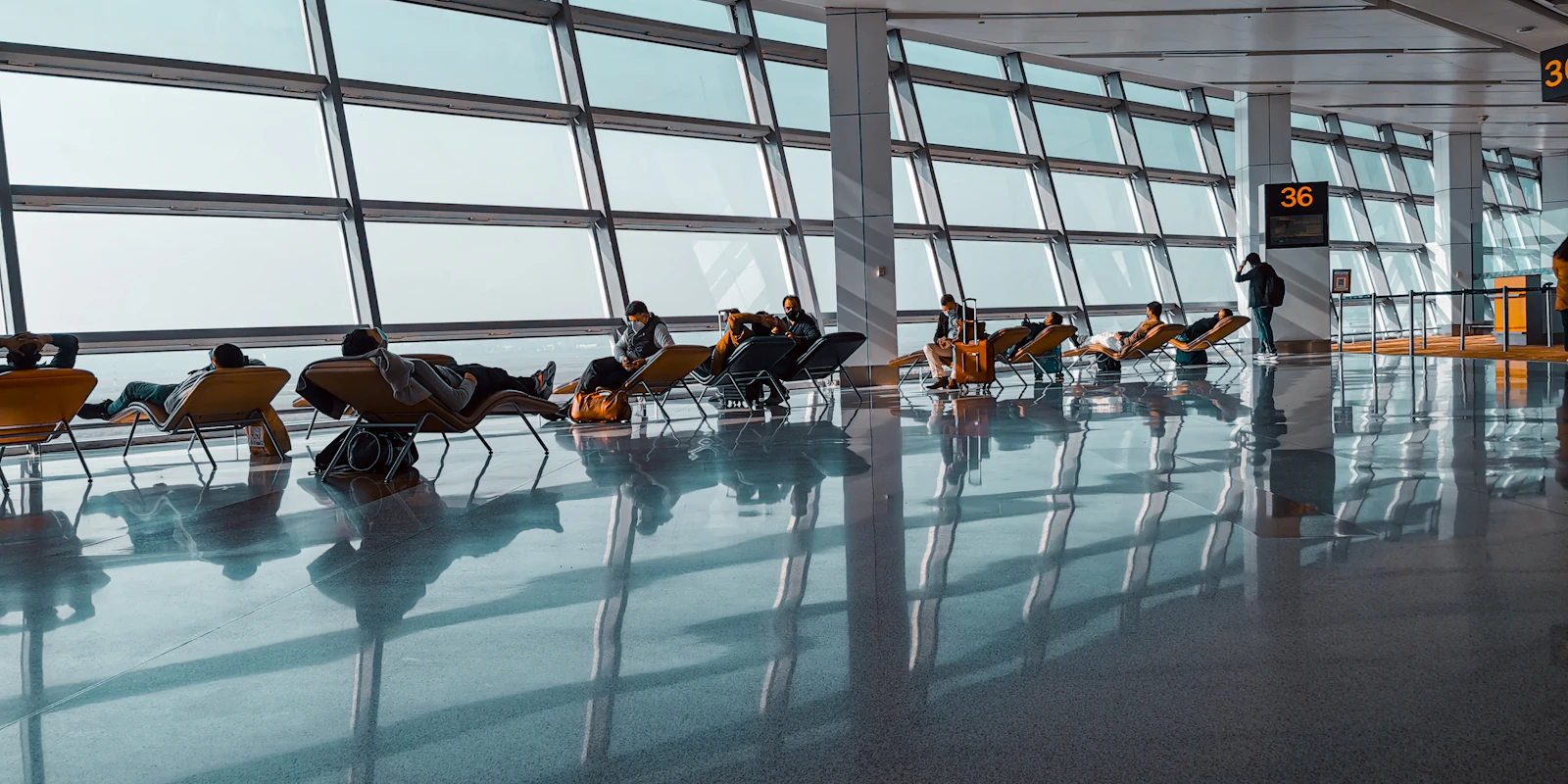 Passengers waiting in a bright airport gate lounge with floor-to-ceiling windows