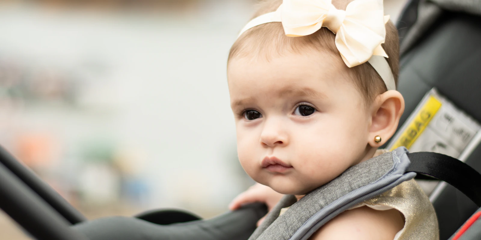 A baby girl with a hair bow sits harnessed into a rear-facing car capsule