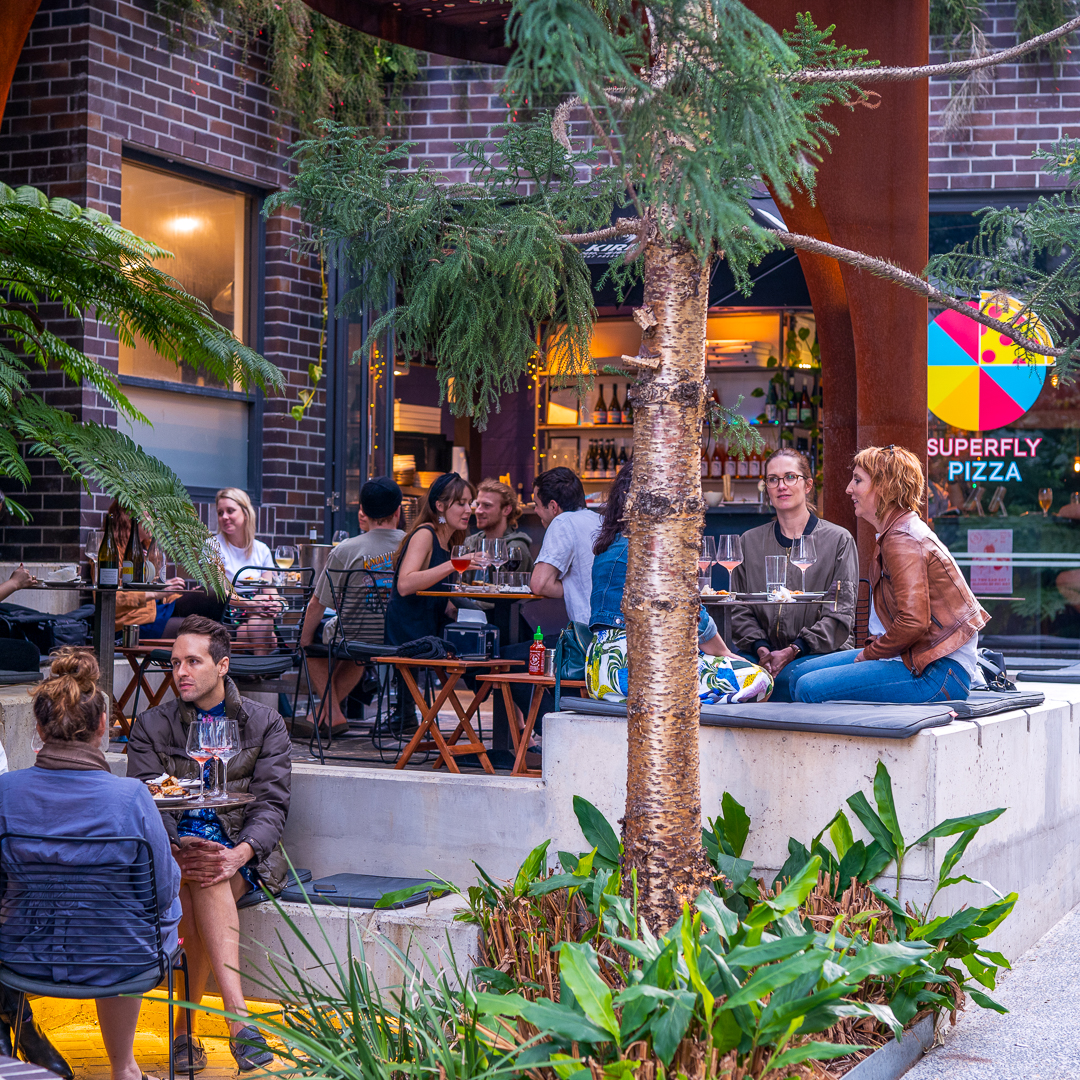 People sitting in a courtyard enjoying wine and pizza