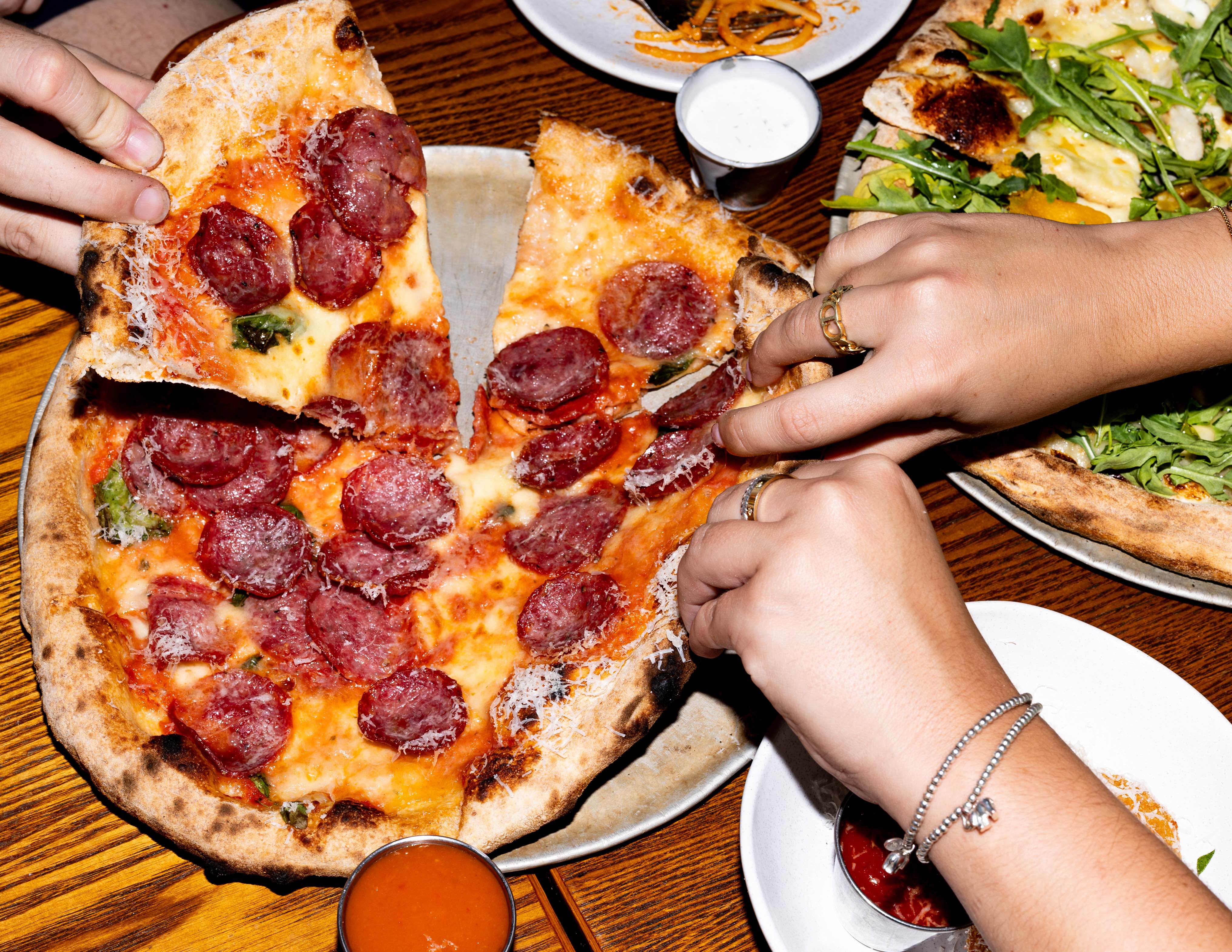 Hands taking pieces of a beautiful pepperoni pizza